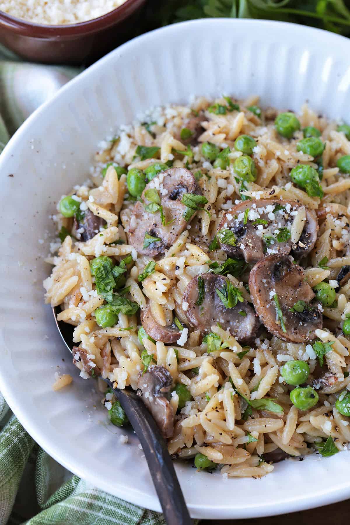 This Creamy Mushroom Orzo with Peas is made with tender pasta, savory mushrooms and sweet peas in a rich, creamy sauce. An easy side dish or a meatless dinner! mushroom and pea orzo in a white bowl with spoon and napkin on the side