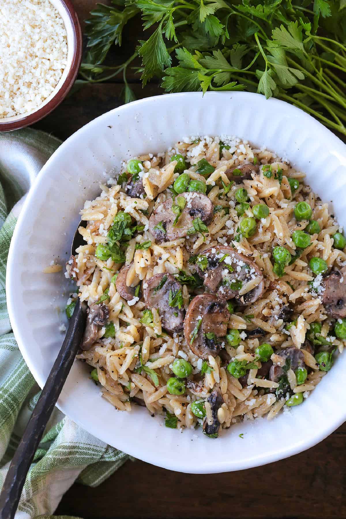 This Creamy Mushroom Orzo with Peas is made with tender pasta, savory mushrooms and sweet peas in a rich, creamy sauce. An easy side dish or a meatless dinner! orzo with mushrooms and peas in a white bowl with spoon
