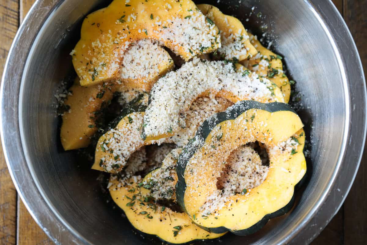 Roasted Parmesan Acorn Squash is so easy to make! Nutty parmesan cheese with fresh thyme is hands down a winning flavor combination. sliced acorn squash in a bowl with parmesan cheese and thyme