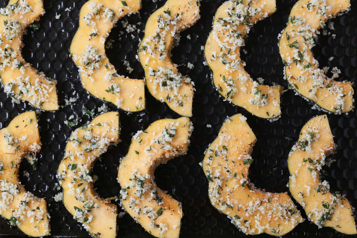 Roasted Parmesan Acorn Squash is so easy to make! Nutty parmesan cheese with fresh thyme is hands down a winning flavor combination. sliced acorn squash on a baking sheet topped with herbs and parmesan cheese