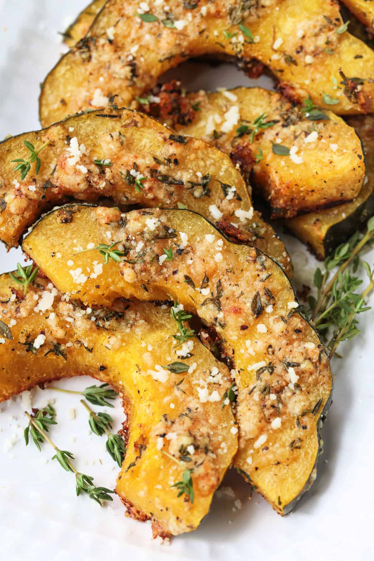 Roasted Parmesan Acorn Squash is so easy to make! Nutty parmesan cheese with fresh thyme is hands down a winning flavor combination. roasted acorn squash on a platter with thyme