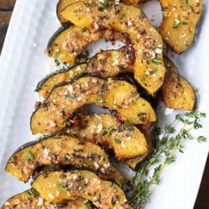 roasted acorn squash slices on a platter with thyme and parmesan cheese